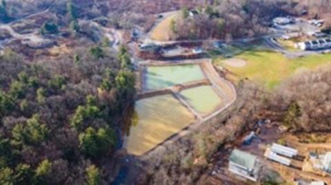 An aerial image shows three water treatment ponds surrounded by forest, field and infrastructure